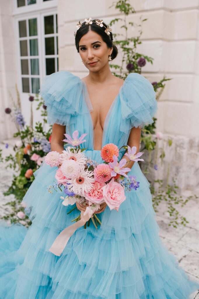 Bride wearing a millia london blue wedding dress and holding colourful bouquet by blooms fair london. 
