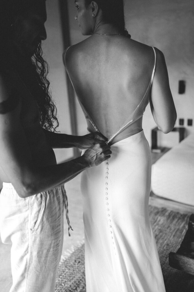 Groom helping bride into her dress before their Tulum wedding. 