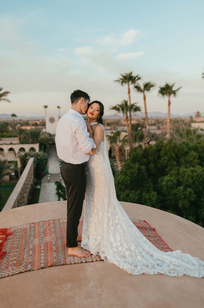 Tigue and Moira hugging after their wedding ceremony standing on rooftop with Palais Namaskar in the background.