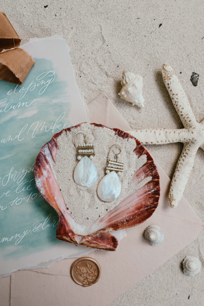 Beach wedding flatlay with stationary, shells and earrings from Freya Rose London. 