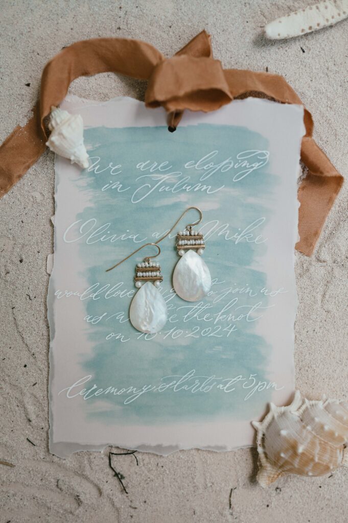 Tulum elopement flatlay with stationary, shells and earrings from Freya Rose London. 