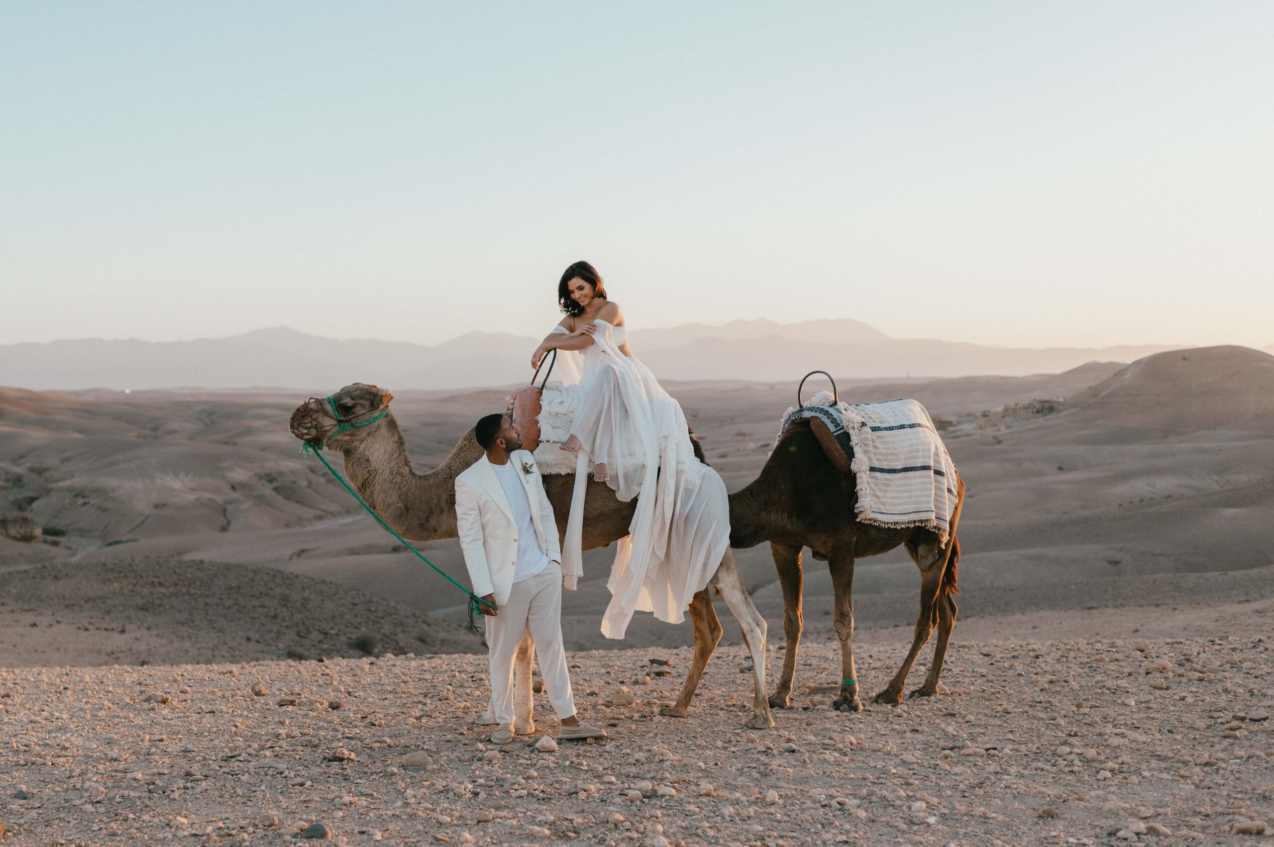 Megan and James with camels in Agafay desert Morocco after their elopement wedding.