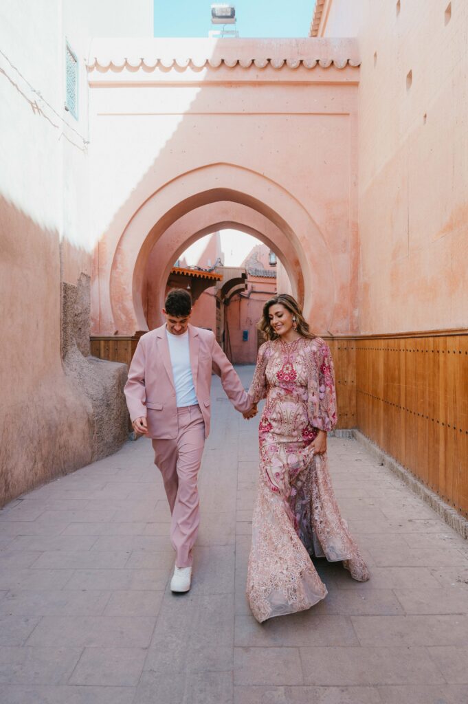 Bride and groom in Marrakech Medina in front of pink arch.