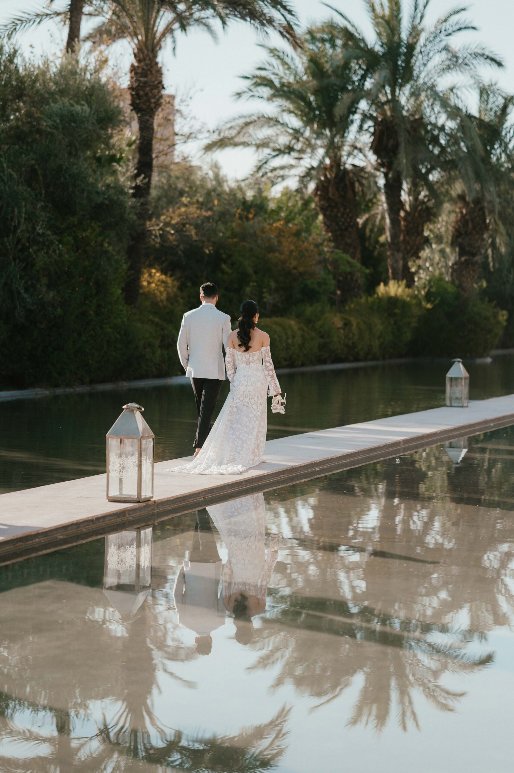 Wide angle of bride and groom walking by the water at Palais Namaskar Marrakech.