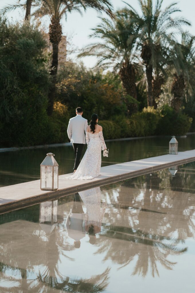 Bride and groom walking on walkway in the water at Palais Nasmakar in Marrakech.