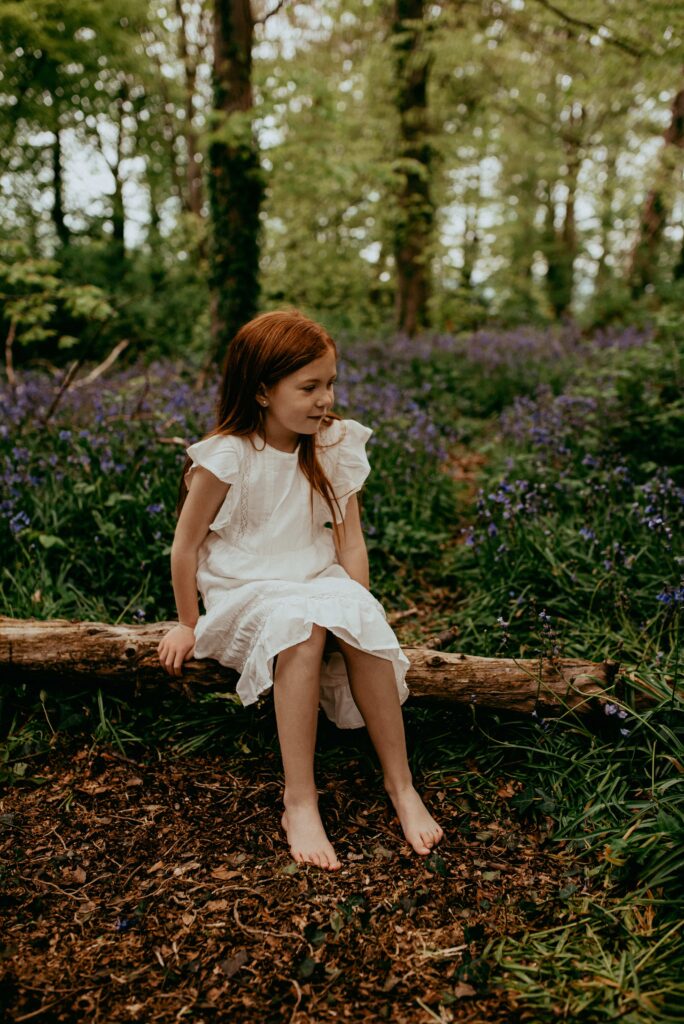 Ginger girl wearing a white Zara dress and sitting on a log in the bluebells woods in Southampton, Hampshire, UK. 