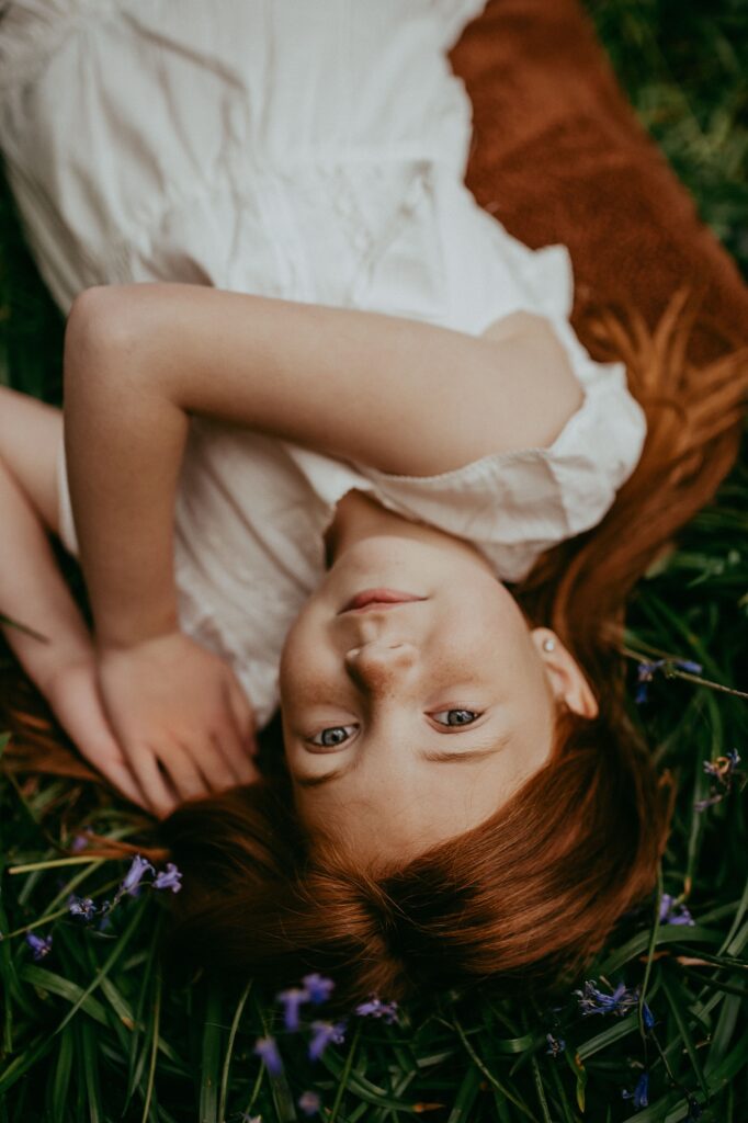 Close up of red hair little girl looking up at the camera and laying down in the bluebells. 