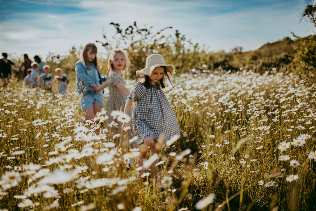 Three girls holding hands and walking amongst the blooming daisies in the field in Portsmouth, Hampshire.