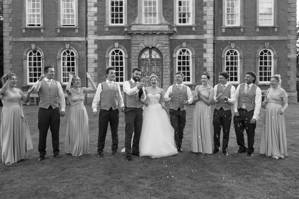 Amanda, John, and their bridal party strolling in front of Kingston Bagpuize House as the evening sun sets, creating a magical atmosphere.