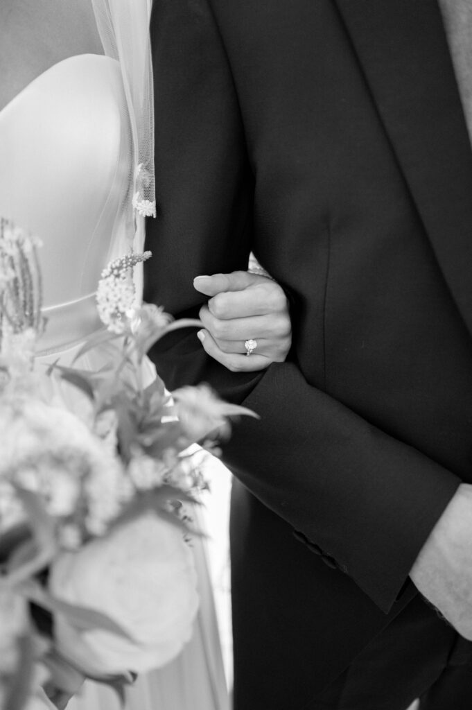 Black and white photo close up of the bride holding her father's arm where we can see her engagement ring.