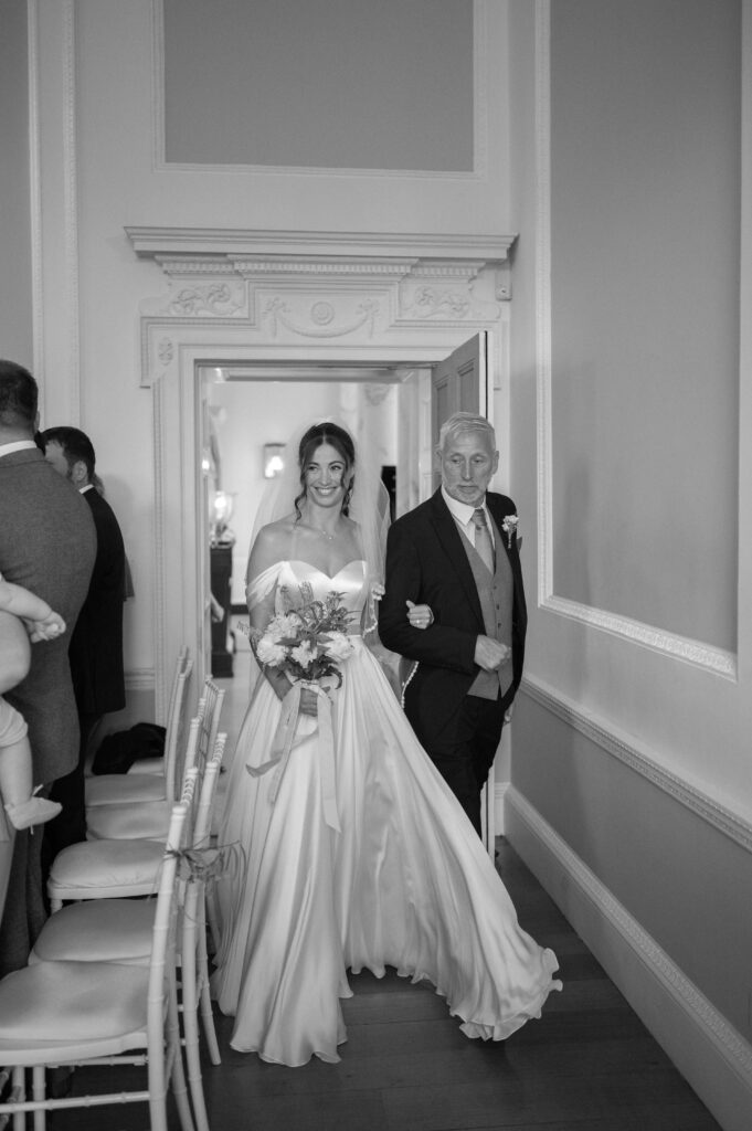 Black and white photo of Charlie waking in the ceremony room with her father.