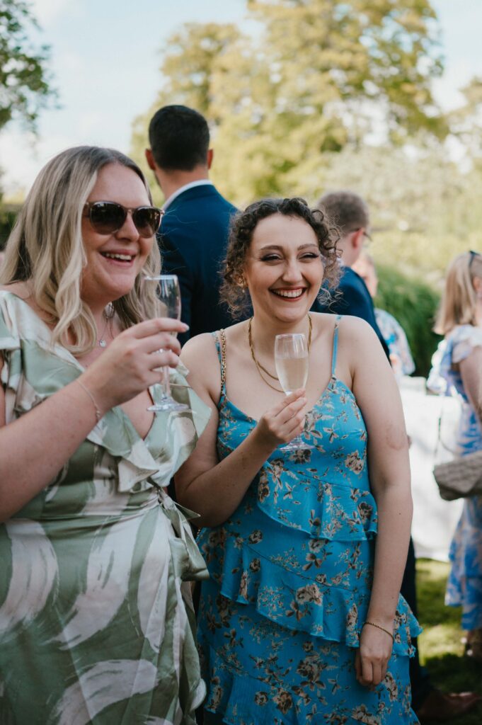 Guests sipping cocktails and enjoying canapés in the sunny garden of Kingston Bagpuize House during the wedding reception.