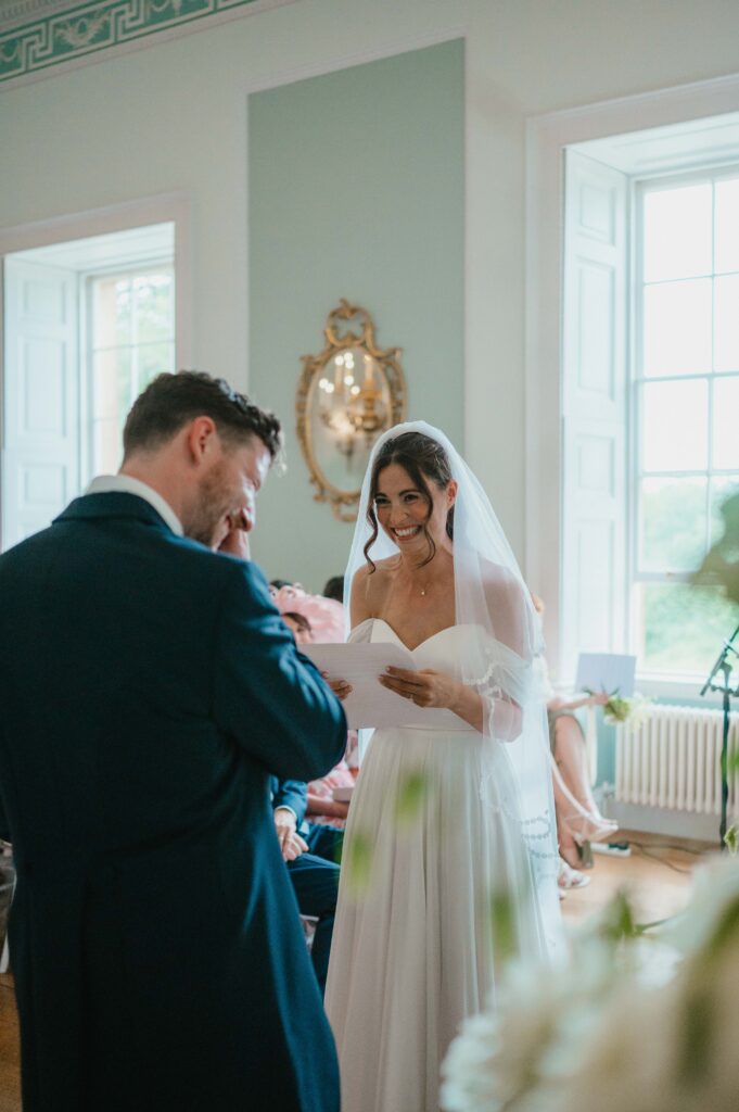 Charlie, the bride, laughing as she reads her vows and Martin wipes away a tear.