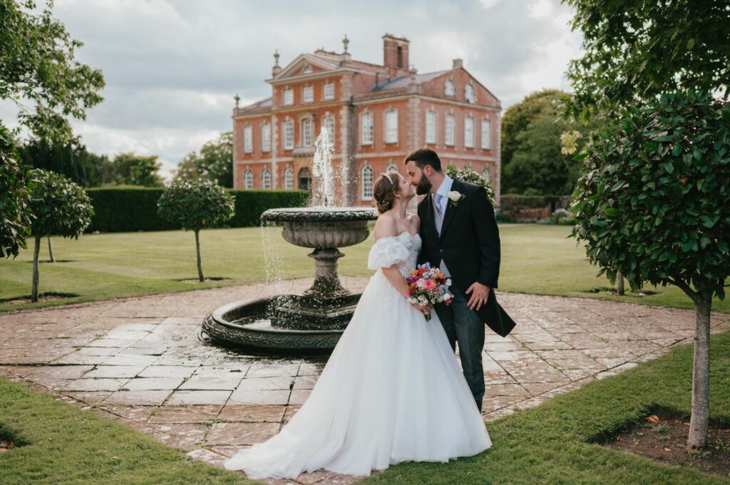 Amanda and John sharing a romantic moment in front of the beautiful fountain at Kingston Bagpuize House, with the stunning venue in the background.