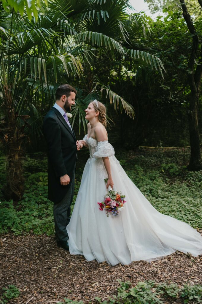 Amanda and John walking hand-in-hand through the lush gardens of Kingston Bagpuize House, with elegant palm trees adding to the scenic backdrop.