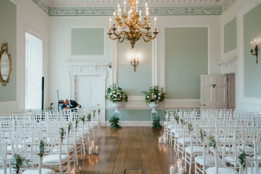 Botleys Mansion's elegant wedding ceremony room with white chairs, floral decorations, and a grand chandelier.