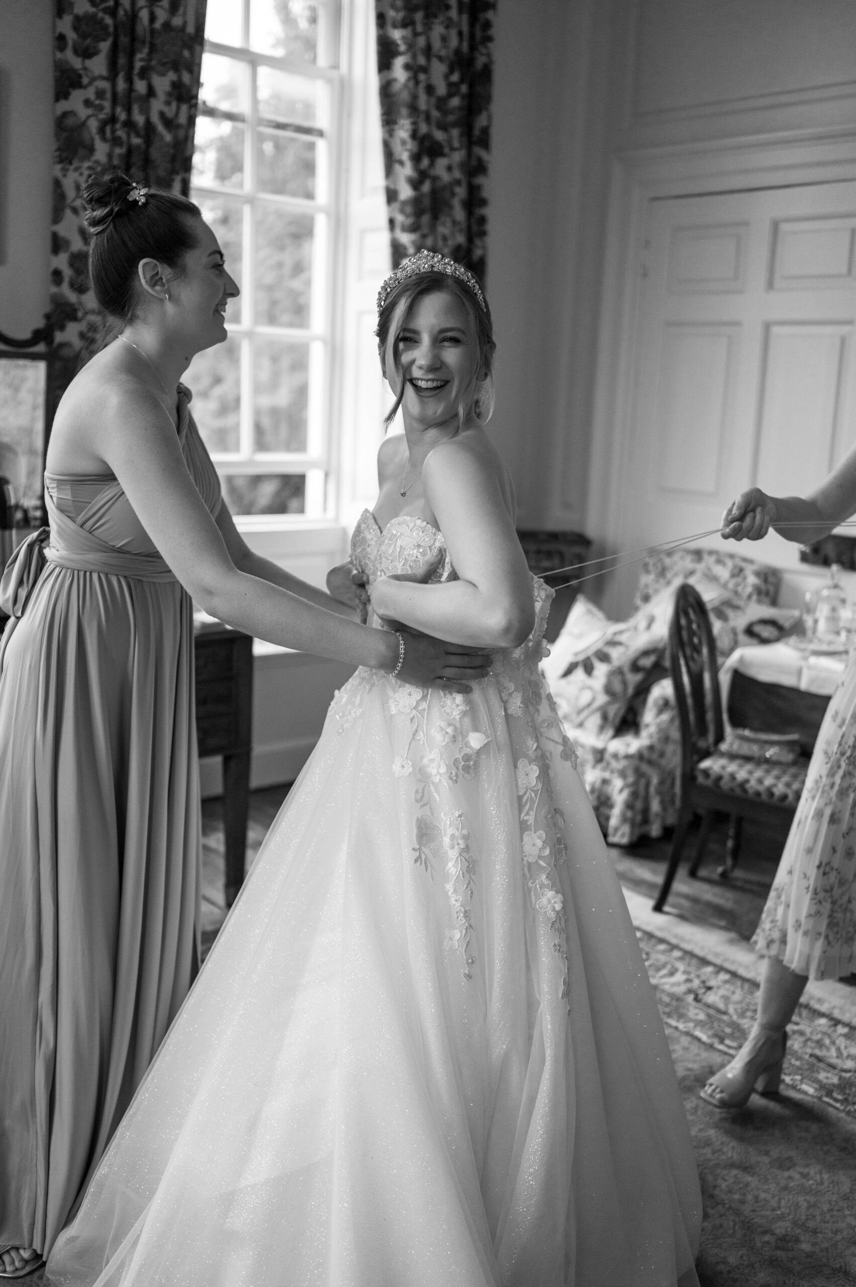 Amanda and her bridesmaids sharing a moment of laughter as they make final adjustments to her wedding dress, full of love and joy.