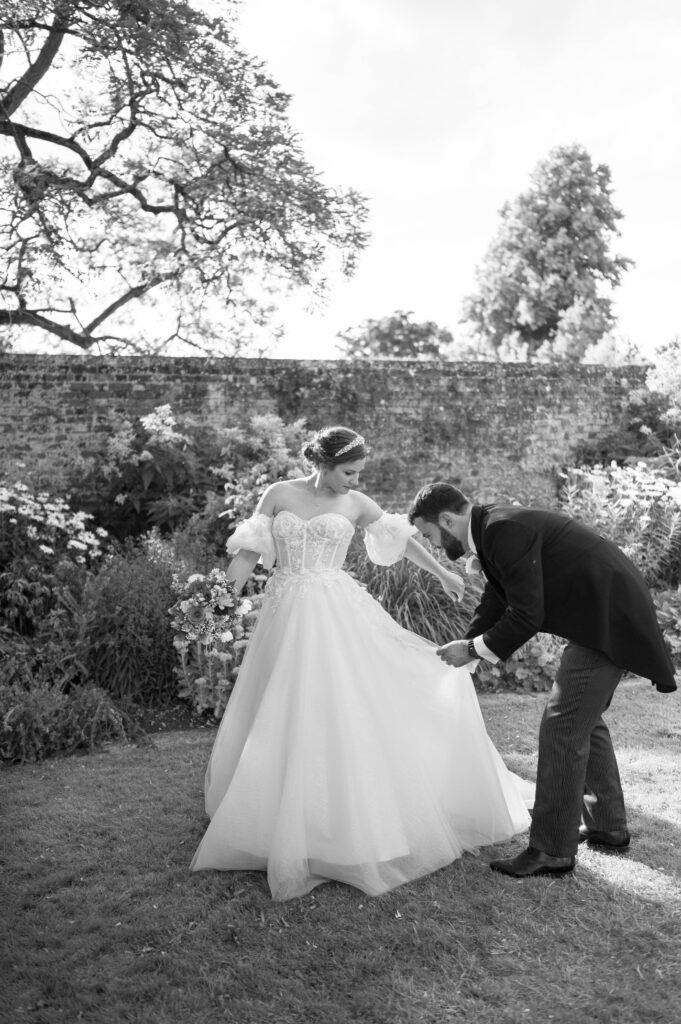 Candid black and white photo of John helping Amanda with her dress in the gardens of Kingston Bagpuize House.