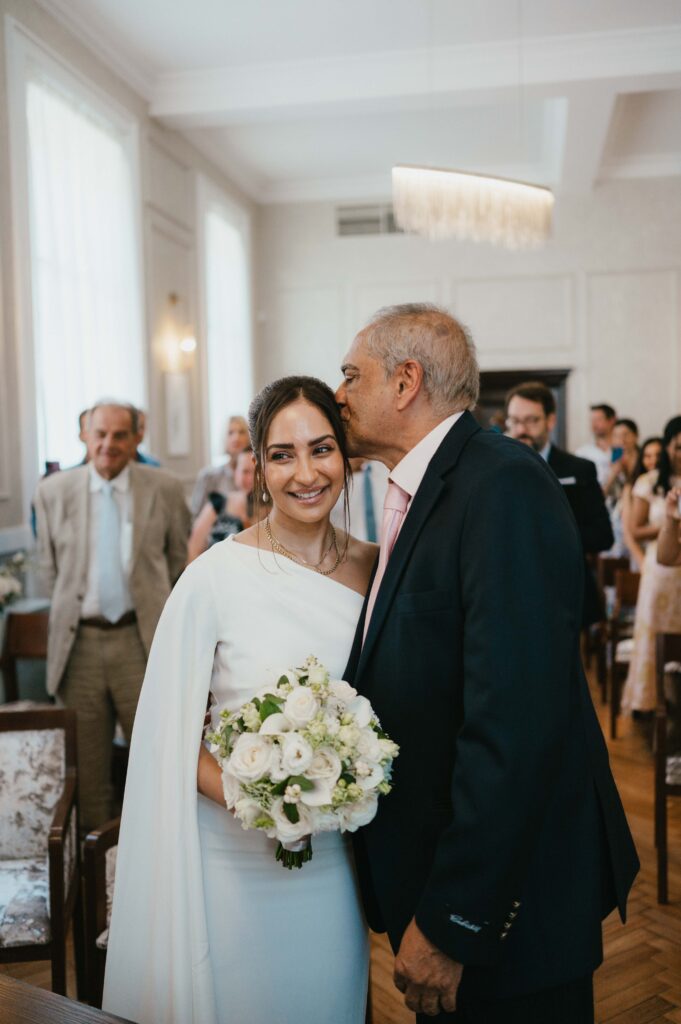 The father of the bride giving away his daughter and giving her a kiss on the head. 