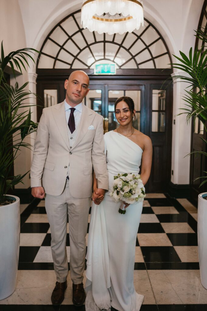 The bride and groom walking out of their ceremony and standing inside the foyer at Chelsea Town Hall.