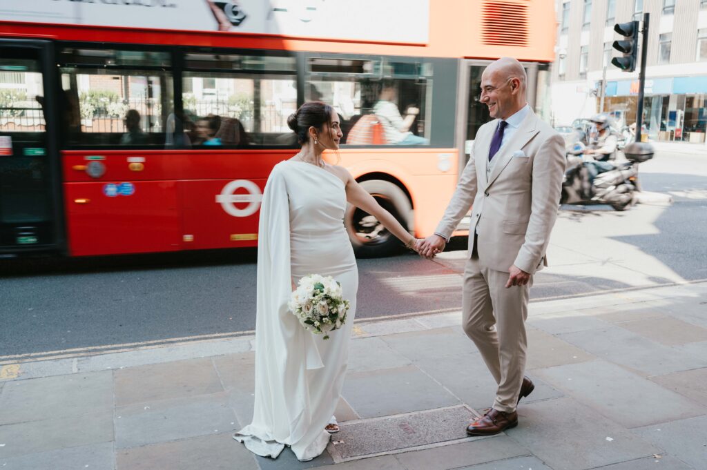 Captured in front of a famous London red bus, Raissa and Vasileios share a joyful moment, celebrating their newlywed status after their Chelsea Old Town Hall wedding.