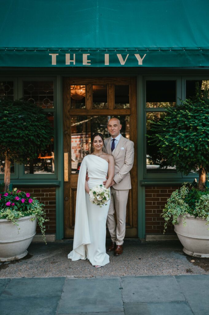 Raissa and Vasileios stand together in front of The Ivy, basking in the joy of their wedding day following their Chelsea Old Town Hall ceremony.