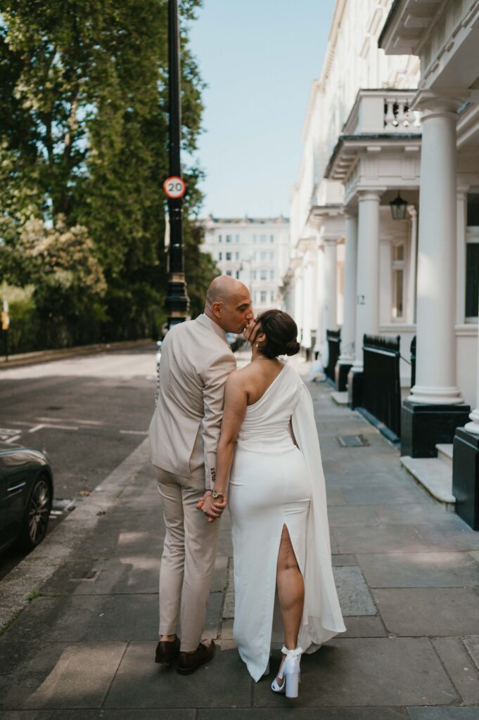 The couple shares a kiss along the peaceful pathways of Warwick Square, surrounded by lush greenery.