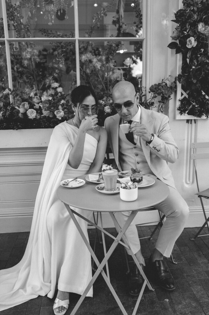 Black of white photo of Raissa and Vsileios sitting at a dainty table adorned with pastel treats. The couple savour their drinks amidst the whimsical charm of Peggy Porschen Café.