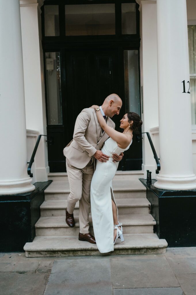 The couple embraces in front of door number 12 at Warwick Square, holding hands and smiling, a symbolic touch for their August 12th wedding date.