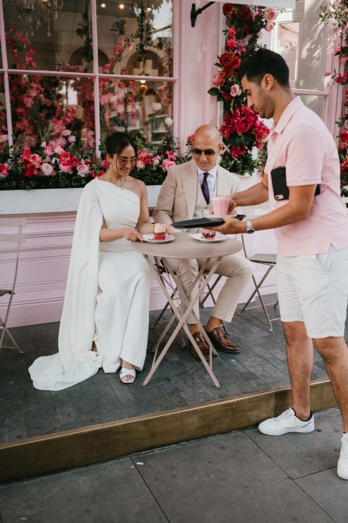 The waiter, wearing a pink polo shirt, at Pergy Porschen Cafe serving Raissa and Vasileios their coffee and cakes.