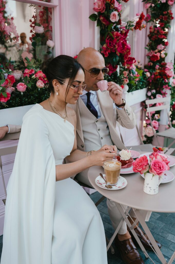 A stylish couple enjoys a romantic moment at Peggy Porschen Café, sipping drinks and surrounded by vibrant pink florals and whimsical elegance.