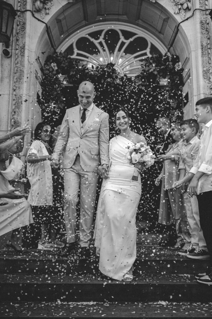 Raissa and Vasileios kiss on the steps Chelsea Old Town Hall, hand in hand, as a shower of confetti rains down in joyful celebration.