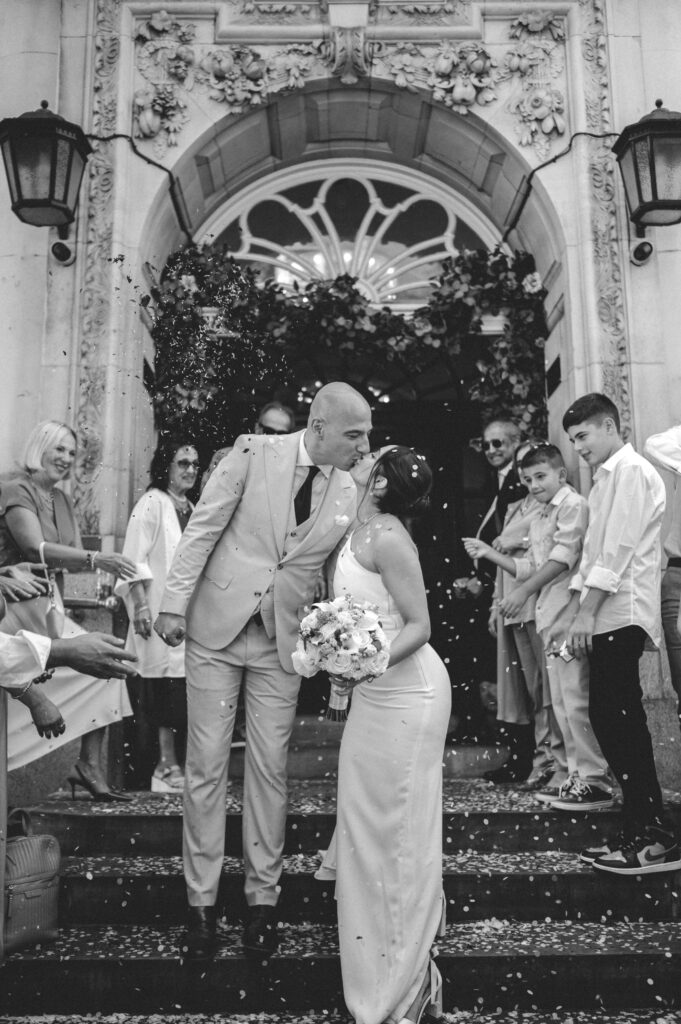 The newlyweds pose in front of Chelsea Old Town Hall’s grand arched entrance, framed by lush red roses.