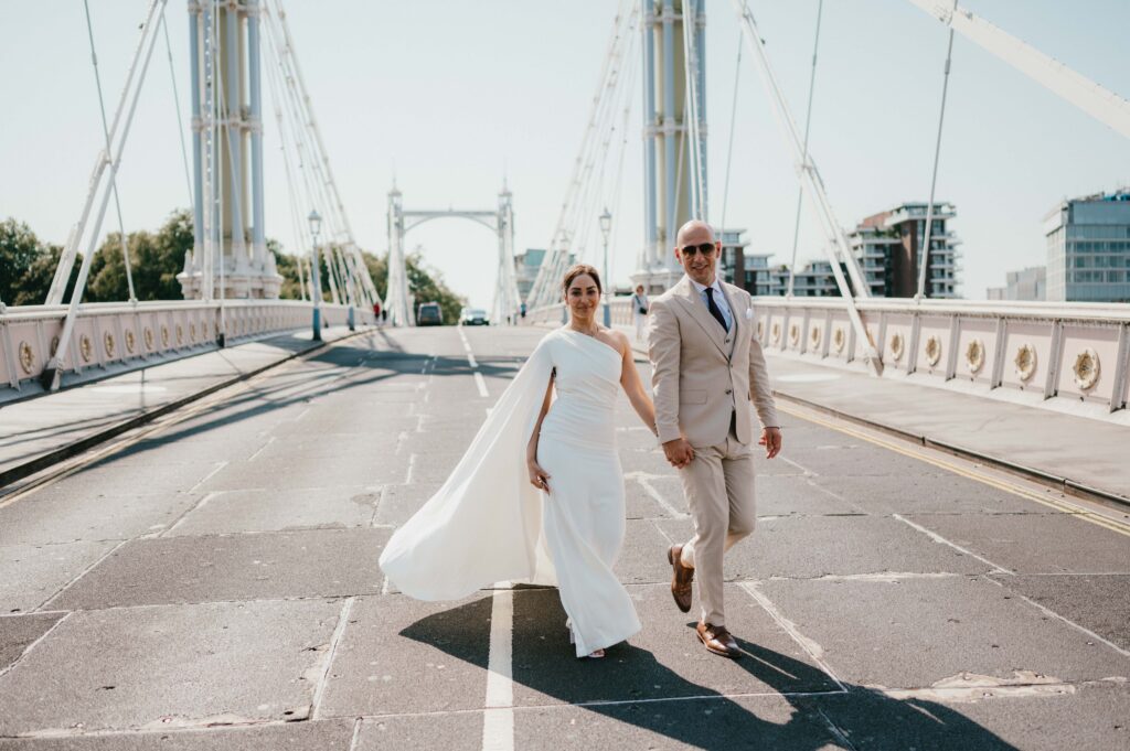 Hand in hand, the couple crosses Albert Bridge, the iconic pastel-hued structure bathed in the golden glow of a summer morning.