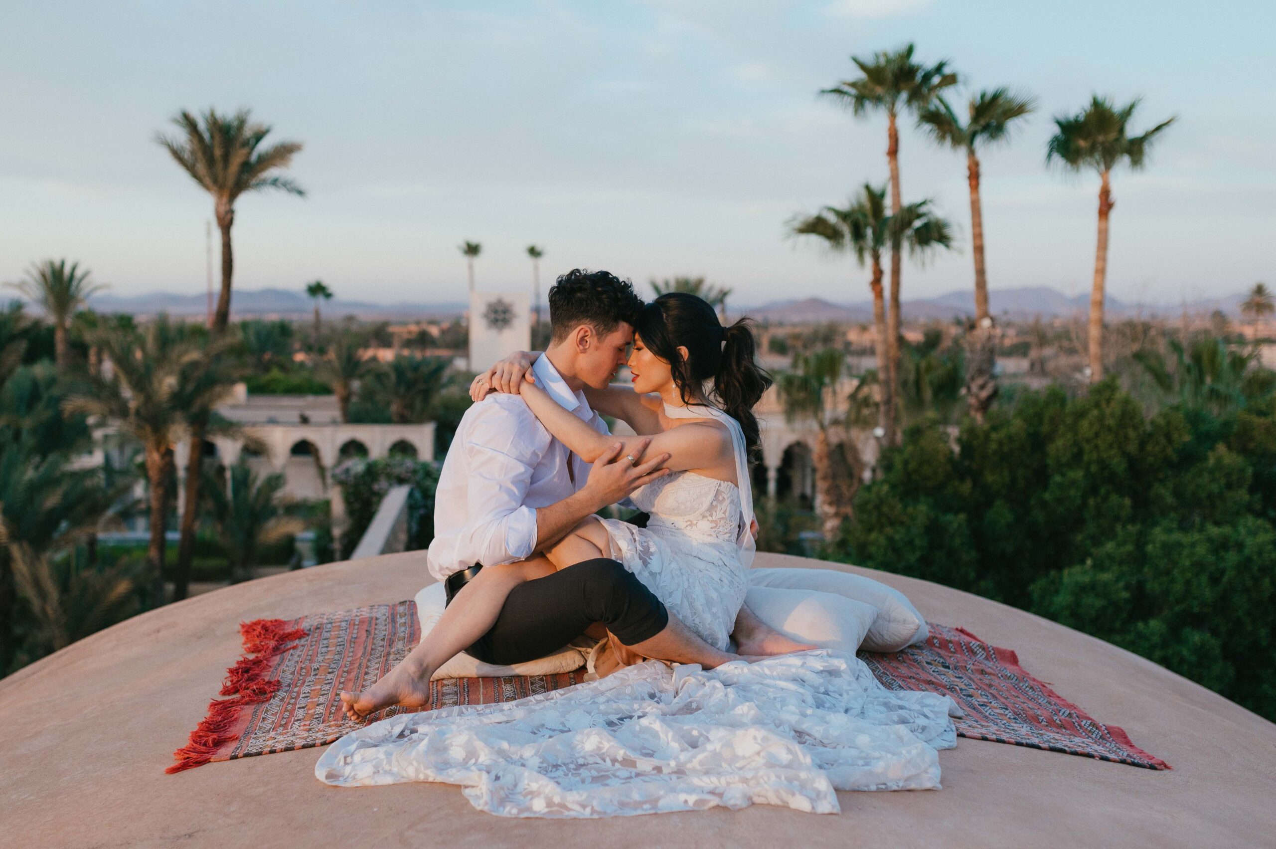 A couple sits on the dome rooftop of the Palais, sharing a kiss with the stunning Marrakech skyline as their backdrop. Captured by Marrakech wedding photographer Sarah Hurja, this intimate moment is filled with love and romance.